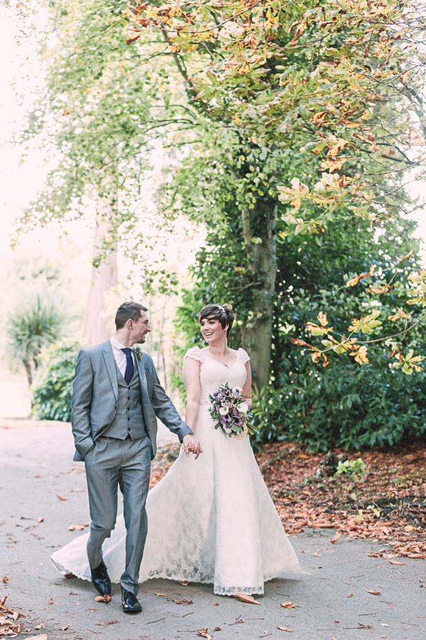 Bride-and-groom-walking-through-highfield-hall-holding-hands-on-autumn-wedding-day-wearing-harriet-wilde-shoes