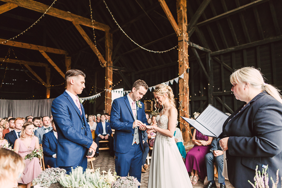 Rustic-barn-wedding-elmley-nature-reserve-bride-and-groom-exchanging-rings-bride-wearing-maggie-sottero-wedding-dress
