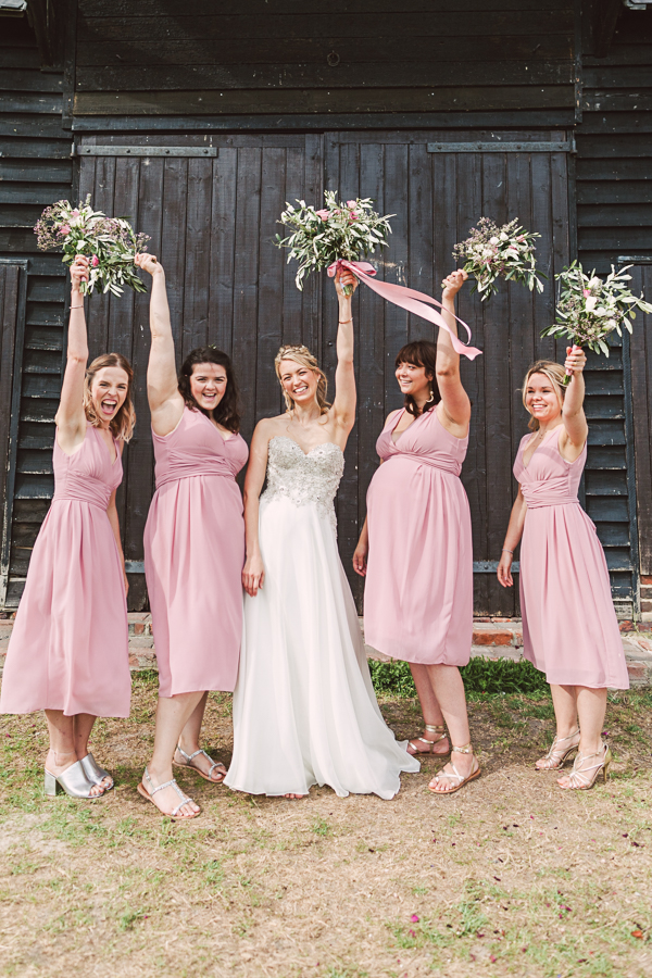 bride-and-bridesmaids-fun-wedding-group-portrait-with-dusky-pink-roses-bouquet-and-olive-branches-elmley-nature-reserve-barn-wedding